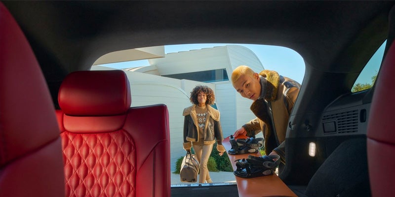 Genesis GV70 red leather interior with a person loading luggage into the rear cargo area.