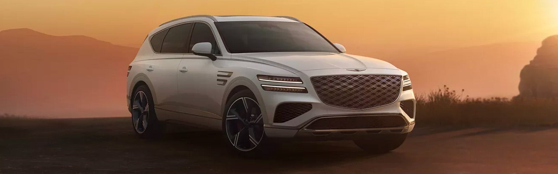 White Genesis GV80 SUV parked on a scenic desert road at sunset.