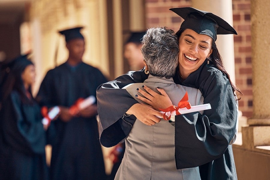 A Woman Graduate Hugging Another Woman Surrounded By Goup Of Student