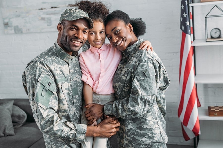 A Military Couple With Their Daughter Standing In Front Of A Wall